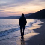 A lone figure walking beside the ocean at dusk, representing reflection and life transitions explored in psychoanalytic therapy.