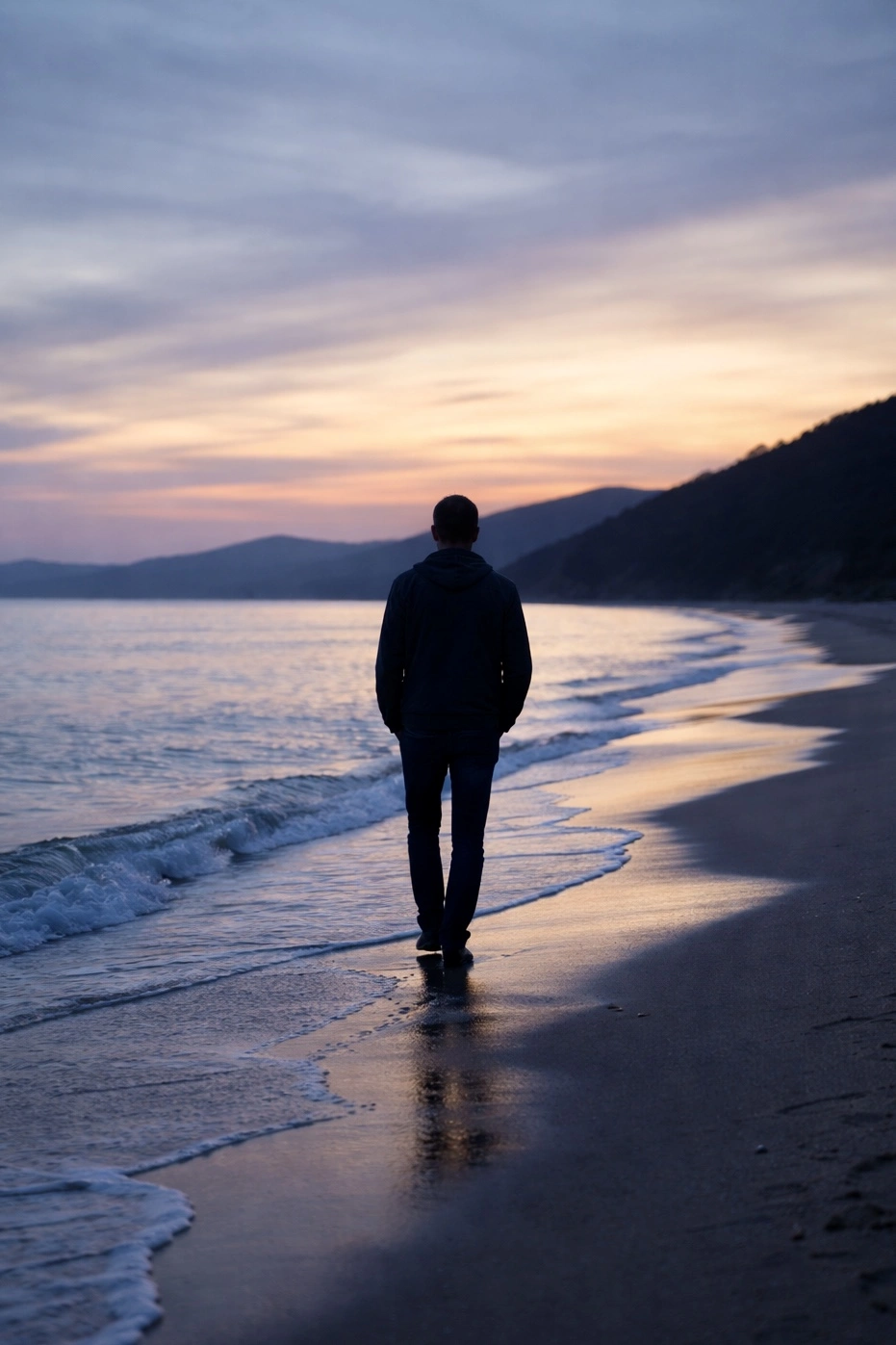 A lone figure walking beside the ocean at dusk, representing reflection and life transitions explored in psychoanalytic therapy.
